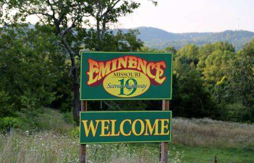 Sign welcoming visitors to Eminence, Missouri, with scenic hills in the background.