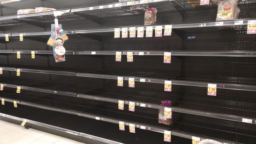Empty supermarket shelves with a few items remaining, showcasing a lack of stock and low inventory.