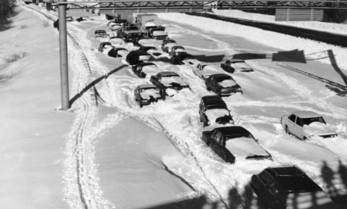 Traffic jam on a snow-covered highway, with cars partially buried in snow.