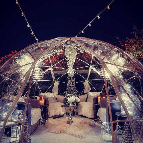A cozy, illuminated igloo-style seating area with plush furniture, candles, and festive decorations at night.