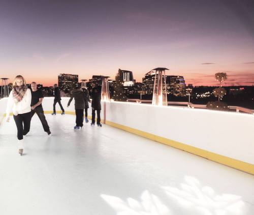 A group of people ice skating at sunset, with city skyline and lights in the background.