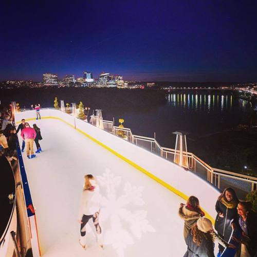 A nighttime ice skating rink with city skyline views, featuring skaters enjoying the activity.