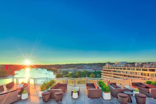 Rooftop view at sunset overlooking a river and city skyline, with modern seating and greenery.