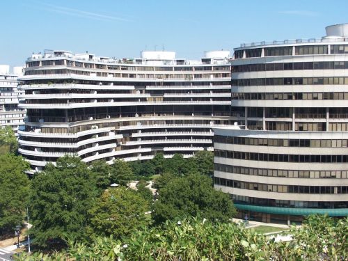 Modern buildings with curved designs surrounded by greenery under a clear blue sky.