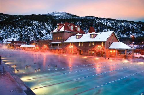 A scenic outdoor pool surrounded by mountains, with steam rising in the winter evening light and a historic building nearby.