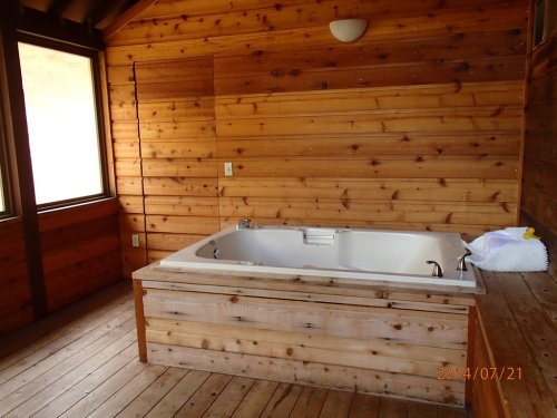A wooden room featuring a white hot tub, wooden walls, and a large window letting in natural light.