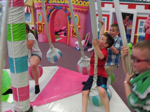 Children playing on colorful swings in a vibrant indoor play area filled with fun structures and decorations.