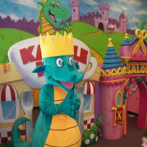 A colorful dragon character wearing a crown stands in front of a whimsical castle-themed backdrop.