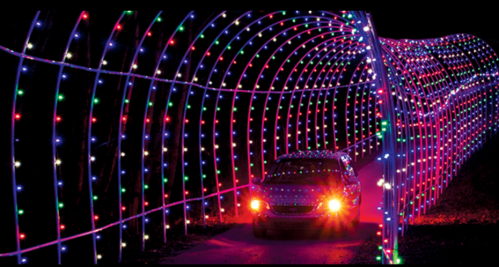 A car drives through a colorful, illuminated tunnel of lights in a dark setting.