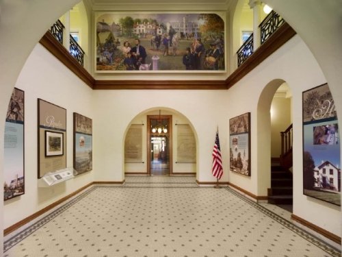 Interior view of a museum hallway featuring murals, informational displays, and an American flag.