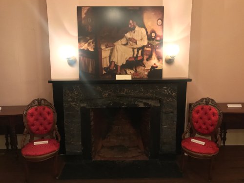 A cozy room featuring a fireplace, two red upholstered chairs, and a large painting above the mantel.