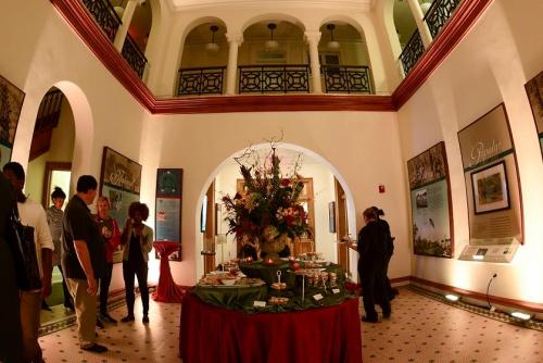 A spacious gallery with a floral centerpiece, guests mingling, and art displays on the walls.