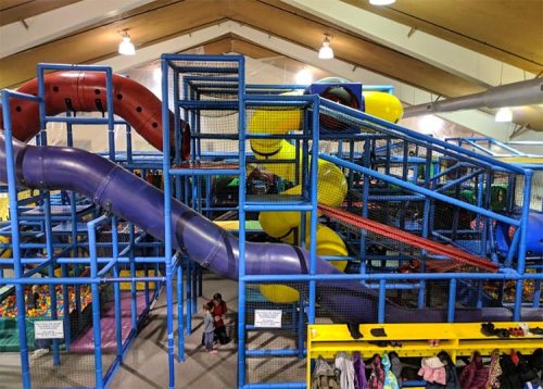 Colorful indoor play structure with slides, climbing areas, and ball pits, bustling with children playing.