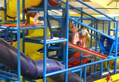 Children play on colorful indoor playground equipment with slides and climbing structures.