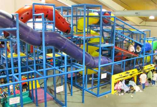 A colorful indoor play structure with slides and climbing areas, filled with children playing and exploring.