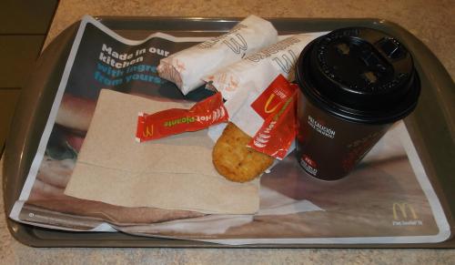 A McDonald's tray with a coffee cup, two wrapped sandwiches, a hash brown, and ketchup packets on a paper placemat.