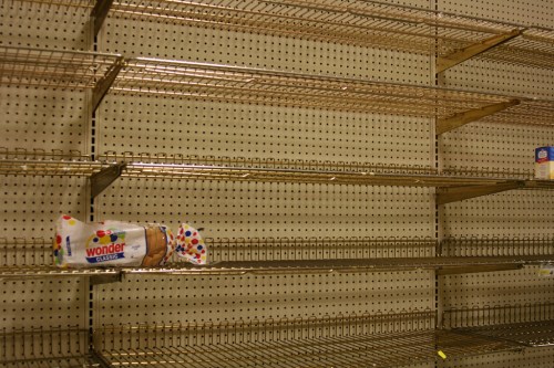 Empty store shelves with a single loaf of Wonder bread on the left side.
