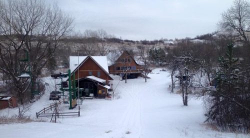 A snowy landscape featuring a rustic cabin and surrounding trees, with a path leading through the winter scenery.