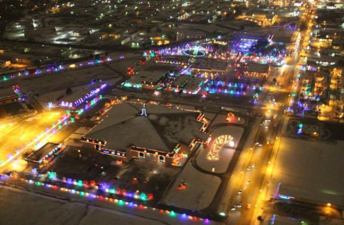 Aerial view of a snowy landscape adorned with colorful holiday lights illuminating buildings and streets at night.
