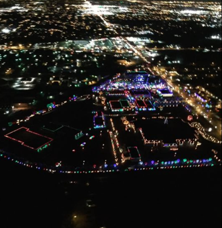Aerial view of a brightly lit area with colorful holiday lights against a dark cityscape at night.