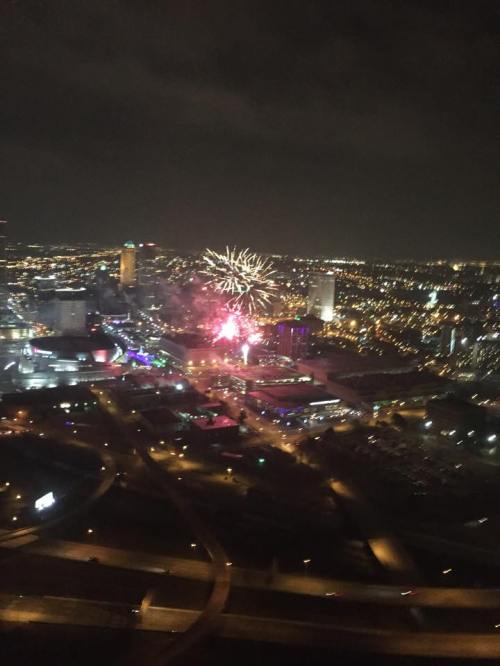 Aerial view of a city at night, illuminated by colorful fireworks against a dark sky.