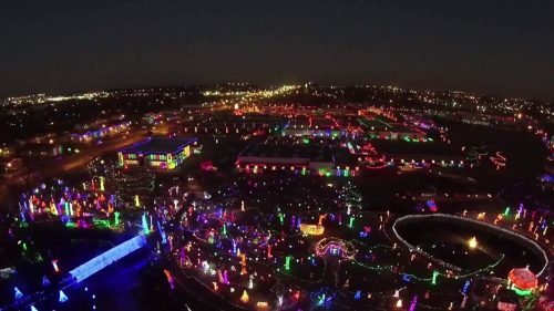 Aerial view of a vibrant holiday light display illuminating a park at night, with colorful decorations and patterns.