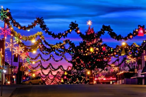 A festive street adorned with colorful Christmas lights and decorations against a vibrant sunset sky.