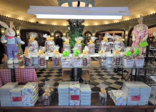 A display of gift baskets and wrapped treats, decorated with ribbons, in a charming shop setting.