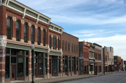 Historic brick buildings line a quiet street under a blue sky, showcasing architectural details and storefronts.