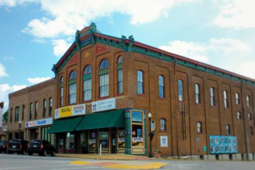 Historic brick building with colorful trim, featuring storefronts and a green awning, under a blue sky.