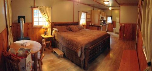 Cozy cabin interior featuring a large bed, wooden furniture, and a kitchenette in a warm, inviting atmosphere.