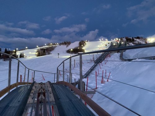 A snowy ski slope illuminated by lights at dusk, with a view from a roller coaster track.