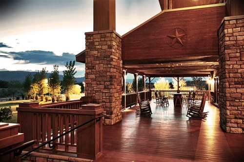 A spacious wooden porch with rocking chairs, overlooking a scenic landscape at dusk.