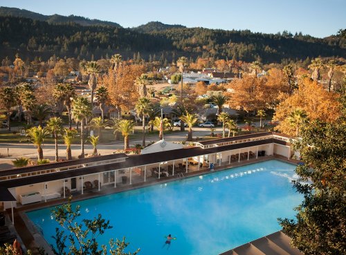 A serene outdoor pool surrounded by palm trees and autumn foliage, with mountains in the background.