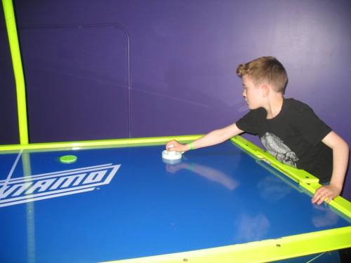 A child plays air hockey, focused on hitting the puck towards the goal on a bright blue table.