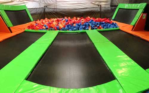 A colorful indoor trampoline park featuring two trampolines and a large foam pit filled with blue, red, and orange blocks.