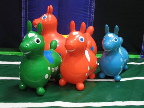 Four colorful inflatable horse toys in green, red, and blue, with playful designs, set against a green and black background.