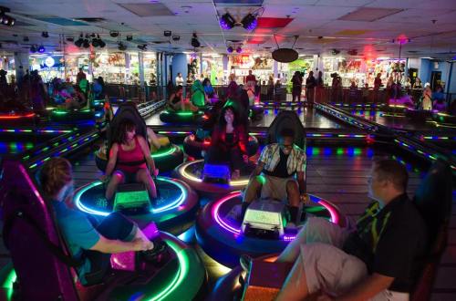A vibrant arcade with people enjoying bumper cars, surrounded by colorful lights and a lively atmosphere.