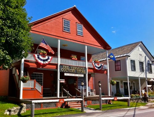 A red country store with flags and bunting, surrounded by green trees and a clear blue sky.