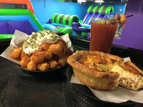 A plate with tater tots topped with sour cream, a quiche, and a cocktail on a table in a colorful play area.