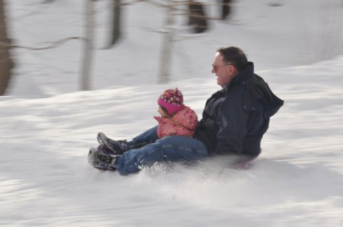 A man and a child sledding down a snowy hill, both smiling and enjoying the winter day.