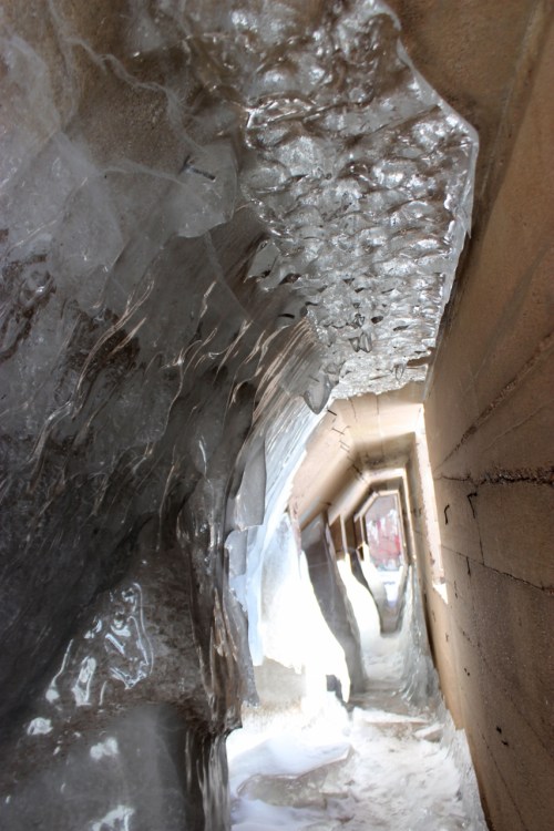 A narrow passageway lined with glistening ice formations and textured stone walls, creating a cool, cavernous effect.