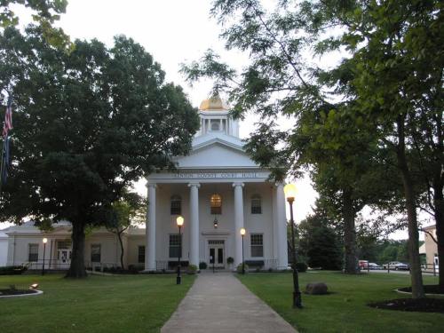 A white building with a golden dome, surrounded by trees and a pathway, featuring columns and outdoor lighting.