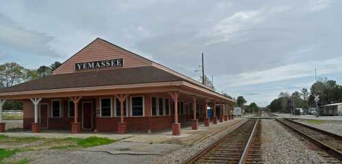 Historic train station in Yemassee, South Carolina, with tracks running alongside and a cloudy sky above.