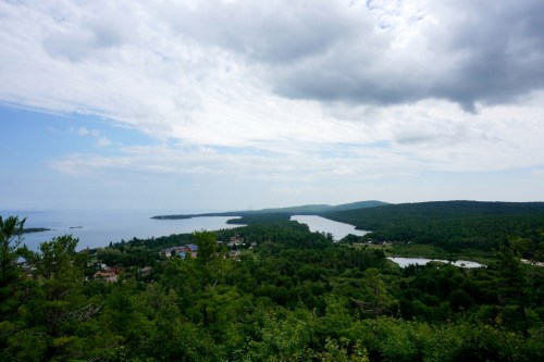 A scenic view of a lush green landscape with a winding river and a cloudy sky over a tranquil lake.
