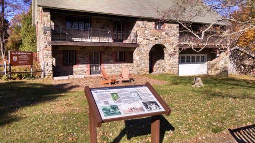A stone building with a sign, surrounded by grass and trees, featuring a display board in the foreground.