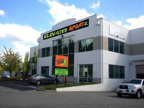 Exterior of a building with "Elevated Sportz" sign, featuring a trampoline park and play area. Cars parked outside.