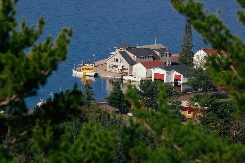 A scenic view of a lakeside community with buildings and a yellow boat docked near the shore, surrounded by trees.