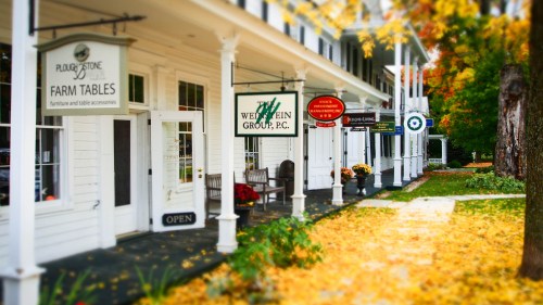 A charming street view featuring shops with signs, surrounded by autumn leaves and colorful foliage.