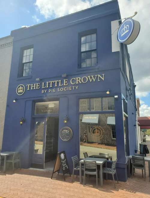 Exterior of "The Little Crown" by Pie Society, featuring a blue facade, large windows, and outdoor seating.